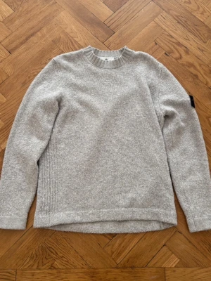 Ljusgrå stickad tröja Stone Island - Ljusgrå stickad tröja från Stone Island med rund halsringning. Knappt använd. Köpt på Jupiter i Stockholm