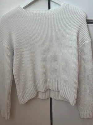 Vit ribbstickad tröja - Mysig vit stickad tröja med ribbad struktur och rund hals. Tröjan har långa ärmar och breda muddar vid ärmslut och nederkant. Perfekt för kyliga dagar och enkel att matcha med olika outfits.