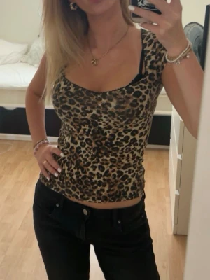 Leopardmönstrad topp - Säljer en croppad topp med leopardmönster. Toppen har en djup rundad urringning och är ärmlös med smala axelband. Materialet känns stretchigt och följsamt, perfekt för dig som vill sticka ut lite extra. Använd nåra gånger men fortfarande i mycket bra skick!