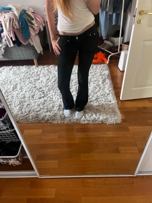 Svarta bootcut jeans - Säljer ett par svarta bootcut jeans med låg midja och klassiska fem fickor. Jeansen har en snygg passform som framhäver benen och är tillverkade i ett stretchigt denimtyg för extra komfort. Jag säljer dem för att de tyvärr är för små i midjan. Dem är långa på mig som är 182 cm. Innerbenslängden är 91 och midjan 35