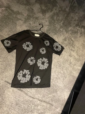 Svart t-shirt med grått mönster - Cool svart t-shirt med unika gråa cirkelliknande tryck över hela plagget. T-shirten har korta ärmar och en klassisk rund halsringning. Perfekt för dig som vill sticka ut med en grafisk look.