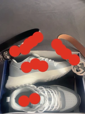 Gråvita chunky sneakers - Snygga chunky sneakers i grått och vitt med tjock sula och perforerad tåbox. Skorna har vita skosnören och detaljer i både läder och textil. Perfekta för dig som gillar en sportig och trendig look.