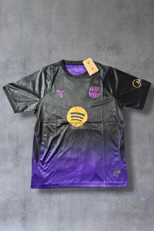 Svart-lila FC Barcelona matchtröja - Snygg FC Barcelona matchtröja i svart och lila med guldfärgade loggor och detaljer. Tröjan har korta ärmar, rund hals och är tillverkad i ett lätt, ventilerande funktionsmaterial. Perfekt för fotboll eller träning.