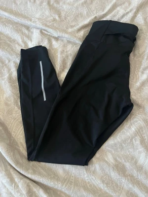 Svarta sportleggings med reflexdetalj - Säljer ett par svarta sportleggings från SOC med hög midja och en snygg reflexdetalj på benet. Tillverkade i stretchigt funktionsmaterial som andas, perfekta för träning eller chill. Diskret logga på höften och smal passform. Storlek M men känns som S🌸