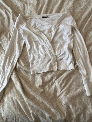 Vit cardigan från Eve, storlek S - Snygg vit cardigan från Eve med v-ringning och knappar framtill. Tröjan har två fickor på framsidan och långa ärmar. Tillverkad i mjukt material som passar perfekt till lager på lager och ger en clean look.