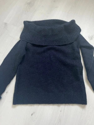 Marinblå off shoulder tröja - Mysig marinblå stickad tröja från Gina Tricot med ribbad offshoulder krage och långa ärmar. Tröjan har en rak passform och ribbade muddar vid ärmslut och nederkant. Perfekt för kalla dagar och enkel att styla till olika outfits.