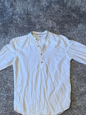 Vit henley-skjorta från Jack & Jones - Säljer en vit henley-skjorta från Jack & Jones i slim fit. Skjortan har lång ärm, rundad halsringning och knappar framtill. Tillverkad i bomull, perfekt för en clean och avslappnad stil.