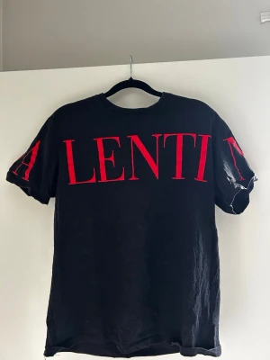 Svart t-shirt från Valentino - Svart t-shirt från Valentino med stora röda bokstäver över bröstet och ärmarna. Klassisk rund halsringning och korta ärmar. Tillverkad i mjuk bomull för en skön och avslappnad look.