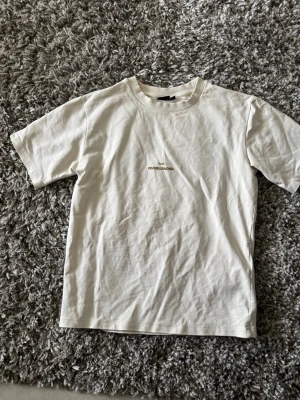 Vit t-shirt med tryck - Snygg vit t-shirt i bomull med minimalistiskt tryck 'OVERLOADED' på bröstet. Klassisk rund halsringning och korta ärmar. Perfekt basplagg för en clean och enkel stil.