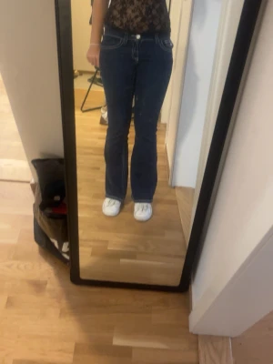 Gina Tricot Mörkblå jeans  - Säljer ett par mörkblå bootcut jeans med vita kontrastsömmar och låg midja. Jeansen har fickor både fram och bak samt bälteshällor. Snygg passform som framhäver benen och ger en retrovibe.