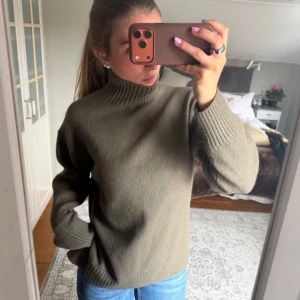 Olivgrön stickad tröja med polokrage - Säljer en stilren olivgrön stickad tröja med hög polokrage och ribbade muddar vid ärmslut och nederkant. Tröjan har en avslappnad passform och är perfekt för lager på lager. Passar till jeans eller kjol för en enkel och snygg look. Från hm💕💕