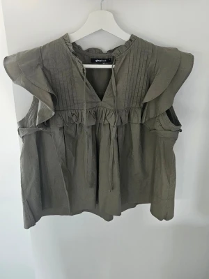Olivgrön blus med volang och knyt - Grön blus från Gina Tricot med volangdetaljer på axlarna, knyt i halsen och fina veck framtill. Köpte den förra året me den har aldrig använts, inte prislappen kvar