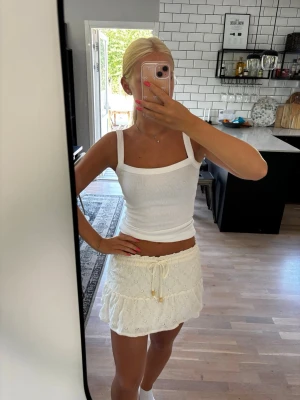 Vit kort kjol med broderade detaljer - Supersöt vit kort kjol med broderade blommor och volang. Kjolen har en dragsko i midjan med knyt. Kjolen har aldrig kommit till användning så prislappen är kvar (se bild) 🌸                        Nypris: 400 kr                                             Publicerad på flera säljsidor 