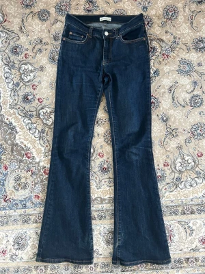 Mörkblå bootcut jeans - Säljer ett par mörkblå bootcut jeans med klassisk femficksdesign och låg midja. Jeansen har utsvängda ben och kontrastsömmar för en snygg retrolook. Perfekta för dig som gillar en tidlös och trendig stil.