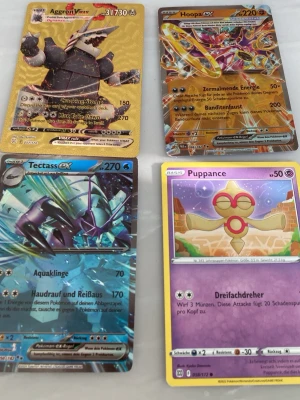 Fyra Pokémonkort GX/EX/Vanliga - Säljer fyra Pokémonkort: Aggron GX (guld), Hoopa GX (färgstark), Tectass EX (blå metallic) och Puppance (lila/gul). Korten har olika coola illustrationer och är tillverkade i glansigt papp. Perfekt för samlare eller Pokémonfans som vill utöka sin kortlek.