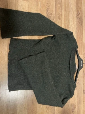 Mörkgrön stickad tröja med vida ärmar - Mysig mörkgrön stickad tröja med bredare, lätt utsvängda ärmar och rund halsringning. Tröjan är lite figursydd. Den är från Gina young 
