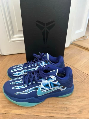 Nike Kobe 6 Protro 'Blue X-Ray' basketsko - Säljer ett par Nike Kobe 6 Protro 'Blue X-Ray' basketskor med blå mesh och syntetmaterial, coolt skelettmönster på ovandelen och turkos sula. Skorna har lågt skaft, klassisk Kobe-logga på plösen och signaturdetalj på hälen. Perfekta för basket eller streetwear.