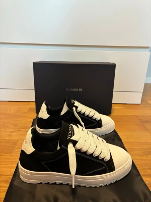 Numeris sneakers  - Stilrena sneakers från Numeris i svart och vitt. Skorna har en chunky sula, breda vita skosnören och detaljer i både mocka och läderimitation. Klassisk låg modell med logga på plösen och hälen. Perfekta för dig som gillar en clean och modern look.