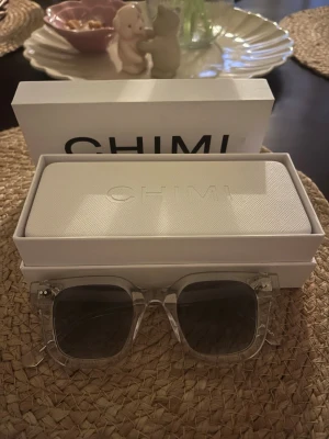 CHIMI 04 - Snygga solglasögon från CHIMI med transparent båge och mörka, fyrkantiga glas. Kommer med original vit hård case och box. Perfekta för dig som vill ha en clean och modern look i sommar.