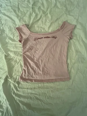 Ljusrosa topp från Gina Tricot - Söt ljusrosa topp från Gina Tricot med texten 'Danser vidue livet' broderad framtill. Toppen har korta ärmar och en bred, något offshoulder ringning. Perfekt för dig som gillar hov1 