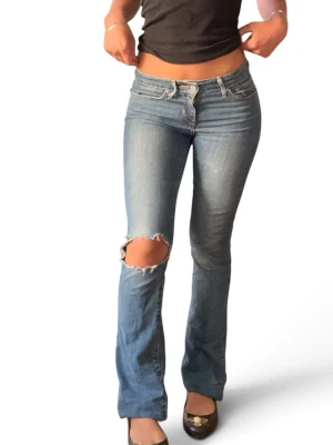 Levis jeans 715 bootcut - Snygga blå bootcut jeans med ett stort slitet hål över vänster knä. Modellen 715 bootcut. Midja rakt över: 37 cm innerbenslängd: 82cm