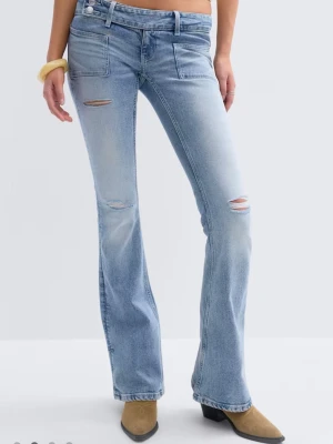 Lågmidjade jeans - Säljer ett par ljusblå bootcut jeans med slitna detaljer och råa hål på låret och knät. Jeansen har framfickor och en klassisk femficksdesign. Perfekt för dig som gillar en avslappnad och trendig look. Petite längd