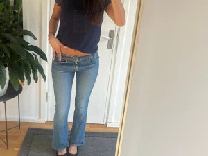 Blåa jeans - Säljer ett par ljusblå jeans med bootcut-modell och låg midja. Jeansen har klassisk femficksdesign och stängs med dragkedja och knapp. Perfekta för en avslappnad och trendig look.