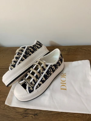  Oblique låga plattform Walk”n”dior sneakers 38 - Snygga låga sneakers från  med klassiskt blått och beige oblique-mönster. Skorna har vita gummisulor, vita tåhättor och matchande vita snören med Christian Dior-logga. Tillverkade i canvasmaterial med exklusiv känsla och detaljerade sömmar.