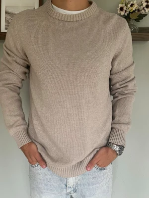 Dobber Stickad Tröja Beige M - Dobber stickad tröja i beige med stilren och klassisk design. Rund hals och ribbade muddar vid hals, ärmar och nederkant. Enkel och lättmatchad modell som passar perfekt till jeans eller chinos.  Skick: fint skick, inga hål eller fläckar Storlek: M Modell: 175 cm / 65 kg — sitter true to size på bild