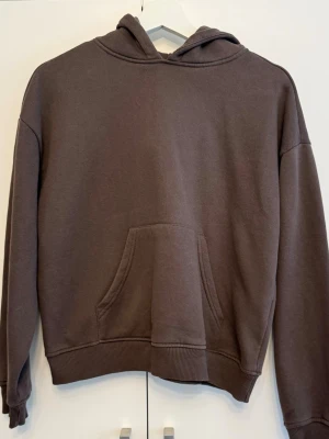 Hoodie  - En brun hoodie med huva och stor magficka framtill. Hoodien har ribbade muddar vid ärmslut och nederkant samt en avslappnad passform. Perfekt för en chill och avslappnad look.