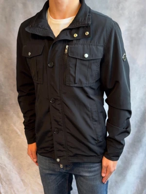 J.Lindeberg Fieldjacket Bailey - Stl M - Riktigt snygg Vår/Höst Bailey Fieldjacket från J-Lindeberg i färgen svart! | Mycket bra skick: 9/10, inga defekter | Stl: M, modellen är 178cm och väger 78kg, passar bra mellan 178-190cm 🙌  | Hör av dig vid frågor // Galgen 🫡