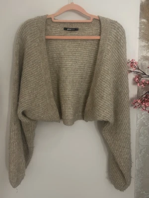 Beige stickad bolero från Gina Tricot - Säljer en beige stickad bolero från Gina Tricot. Modellen är kort och har vida, långa ärmar!