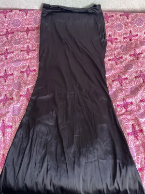 Svart satin kjol - Elegant svart satin kjol. Har en figurnära passform upptill och faller snyggt nedtill. Perfekt för dig som vill ha en stilren och klassisk look. Storleken är M men passar mig perfekt jag som har S🥰är man 177 cm skulle gissa den går vägen ner, väldigt lång är den!😊