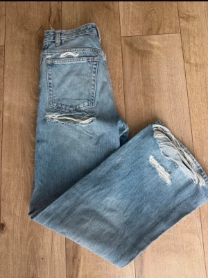 Baggy Zara jeans med hål  - Säljer ett par ljusblå jeans med baggy passform  och tydliga slitningar på både fram- och baksida av benen. Jeansen har klassisk femficksmodell och hög midja. Perfekta för en avslappnad och trendig look. 🩷 Köpta på vinted helt nya men passade tyvärr inte.