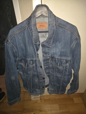 Blå jeansjacka från Levi's XL - Klassisk blå jeansjacka från Levi's i modell 70550. Jackan har två bröstfickor med lock och knappar framtill. Snygga kontrastsömmar och en avslappnad passform som passar perfekt till streetwear-looken.