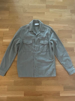 Grön overshirt i manchester från ASOS - Säljer en grön overshirt i mjuk manchester från ASOS DESIGN. Skjortan har två bröstfickor med lock och knappar framtill. Perfekt lager på lager-plagg med avslappnad passform och klassisk krage. XS men passar som S.