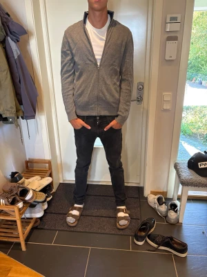 Grå ziptröja med ståkrage - Snygg grå ziptröja med ståkrage och hel dragkedja framtill. Tröjan har ribbade muddar vid ärmslut och nederkant samt en enkel, stilren design. Perfekt att slänga på sig över en t-shirt för en avslappnad look.