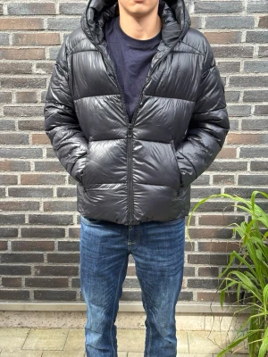 Svart pufferjacka med huva - Säljer en svart pufferjacka med huva och dragkedja framtill. Jackan har två stora fickor på sidorna och breda, vadderade paneler som ger en riktigt puffig look. Perfekt för kalla dagar och riktigt skön att bära. Passar dig som gillar en stilren och enkel vinterjacka.. Skriv gärna vid frågor! Modell:180/70kg