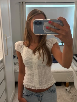 Vit sommartopp med volangdetaljer - Supersöt vit blus med volangdetaljer. Blusen har korta puffärmar som man både man ha på axeln och offshoulder. Också ganska tajt i passformen runt midjan och sitter så fint 💕