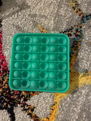 Turkos fyrkantig pop it-leksak - En turkos pop it-leksak i mjukt silikonmaterial. Den är fyrkantig och har flera rader med bubblor att trycka på, perfekt för att sysselsätta händerna eller stressa ner. Enkel att ta med sig och använda när som helst.