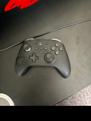 Svart handkontroll från GuliKit - Säljer en svart trådlös handkontroll från GuliKit med ergonomisk design och mattsvart finish. Kontrollen har två analoga spakar, styrkors, klassiska knappar och axelknappar i silverfärg. Perfekt för gaming på konsol eller PC.
