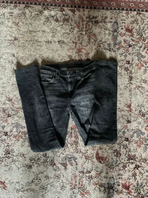 Svarta slim fit Nudie jeans co  - Snygga svarta slim fit jeans med klassisk femficksmodell och diskreta slitningar. Jeansen har normal midja och smala ben, perfekta till en avslappnad men ändå stilren look. Tillverkade i ett stretchigt denimtyg för extra komfort.