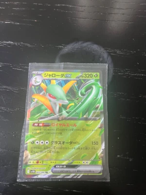 Japansk Pokémonkort Serperior EX - Säljer ett japanskt Pokémonkort med Serperior EX, HP 320. Kortet har grön och gul design med holografiska detaljer och japansk text. Det ligger i ett plastfodral och är från Scarlet & Violet-serien, nummer 003/096 RR.