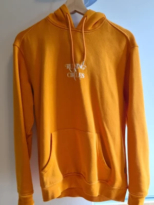 Gul hoodie med tryck Running Circles - Snygg gul hoodie med vit text 'Running Circles' på bröstet. Klassisk känguruficka framtill och justerbar huva med snören. Köpt på Carlings