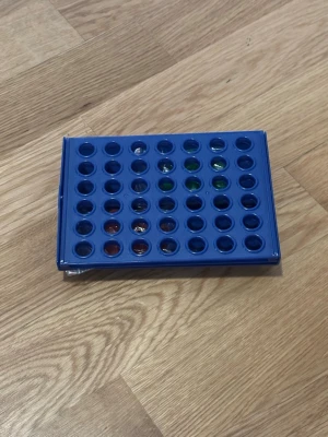 Blått Fyra i rad-spel i plast - Säljer ett klassiskt Fyra i rad-spel i blå plast. Spelplanen har hål för spelbrickor och kommer med röda och gröna marker i plastpåse. Perfekt för två spelare och smidig att ta med på resan eller till spelkvällen.