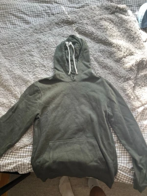 Olivgrön hoodie med ficka och huva - Snygg olivgrön hoodie med klassisk känguruficka framtill och vit dragsko i huvan. Hoodien har långa ärmar och ribbade muddar vid ärmslut och nederkant. Perfekt för en avslappnad och chill stil.