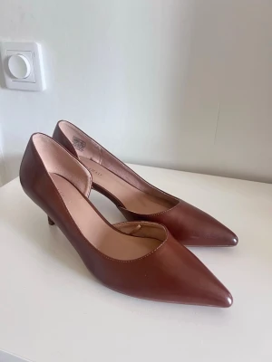 Bruna pumps med låg klack Anna Field - Snygga bruna pumps från Anna Field med spetsig tå och låg klack. Skorna är i ett slätt, glansigt material som ger en elegant look. Skorna är endast använda en gång. 
