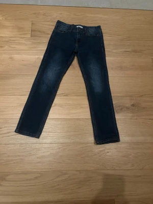 Mörkblå raka jeans från RYLS - Snygga mörkblå jeans från RYLS med raka ben och klassisk femficksmodell. Jeansen har subtila slitningar framtill och kontrastsömmar. Perfekta för en avslappnad och trendig look.