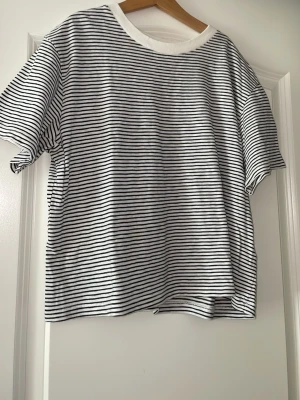 Randig t-shirt från Uniqlo - Säljer en klassisk vit t-shirt med tunna svarta ränder från Uniqlo. T-shirten har rund halsringning med vit ribbad kant och korta ärmar.