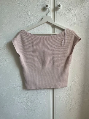 Ljusrosa ribbad croppad topp - Säljer en ljusrosa ribbad topp med v-ringning och korta ärmar. Toppen är croppad och har en mjuk, stretchig känsla som passar perfekt till jeans eller kjol. Enkel men ändå stylish design som är lätt att matcha.